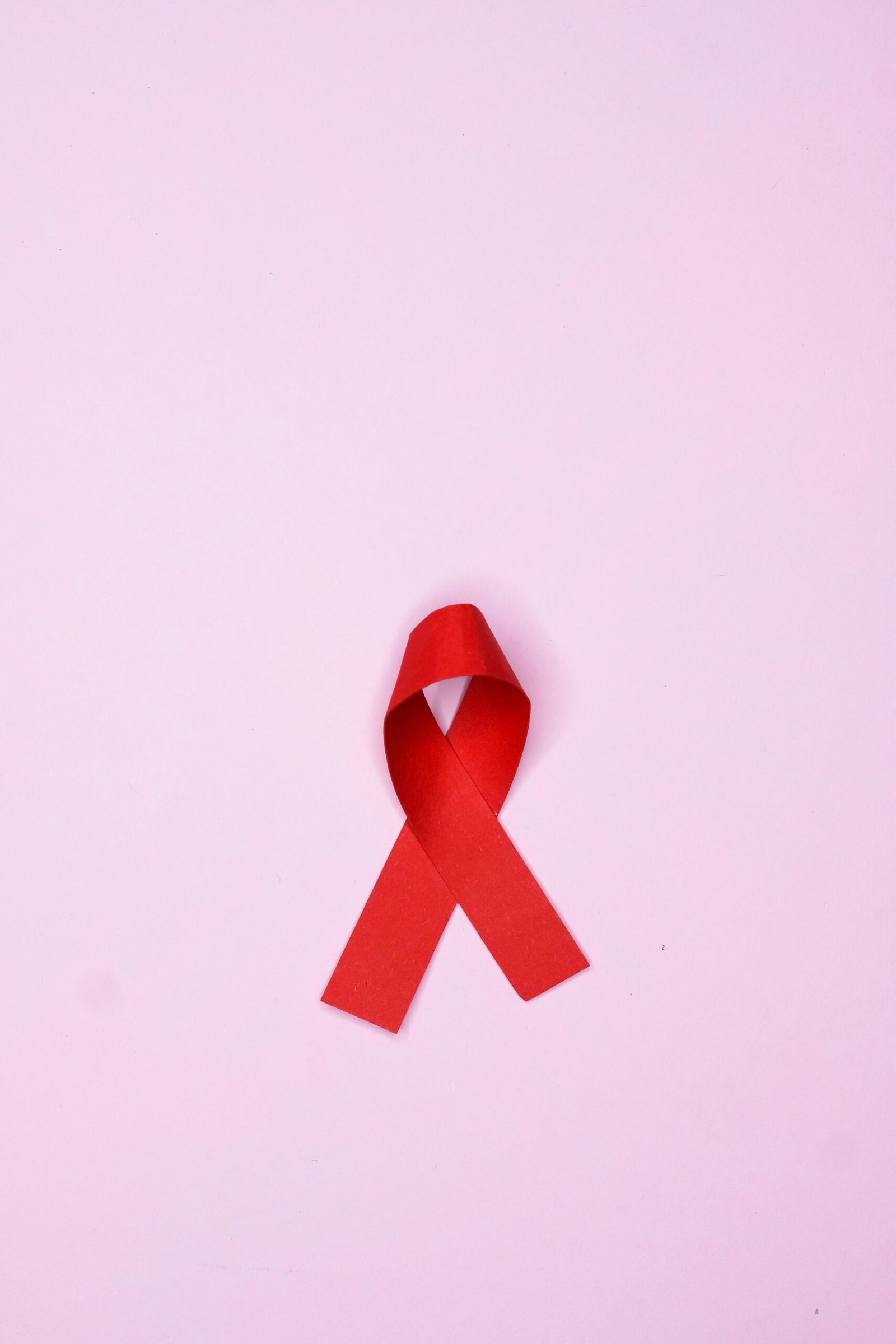 Vertical shot of a red ribbon symbolizing AIDS awareness on a pink background.